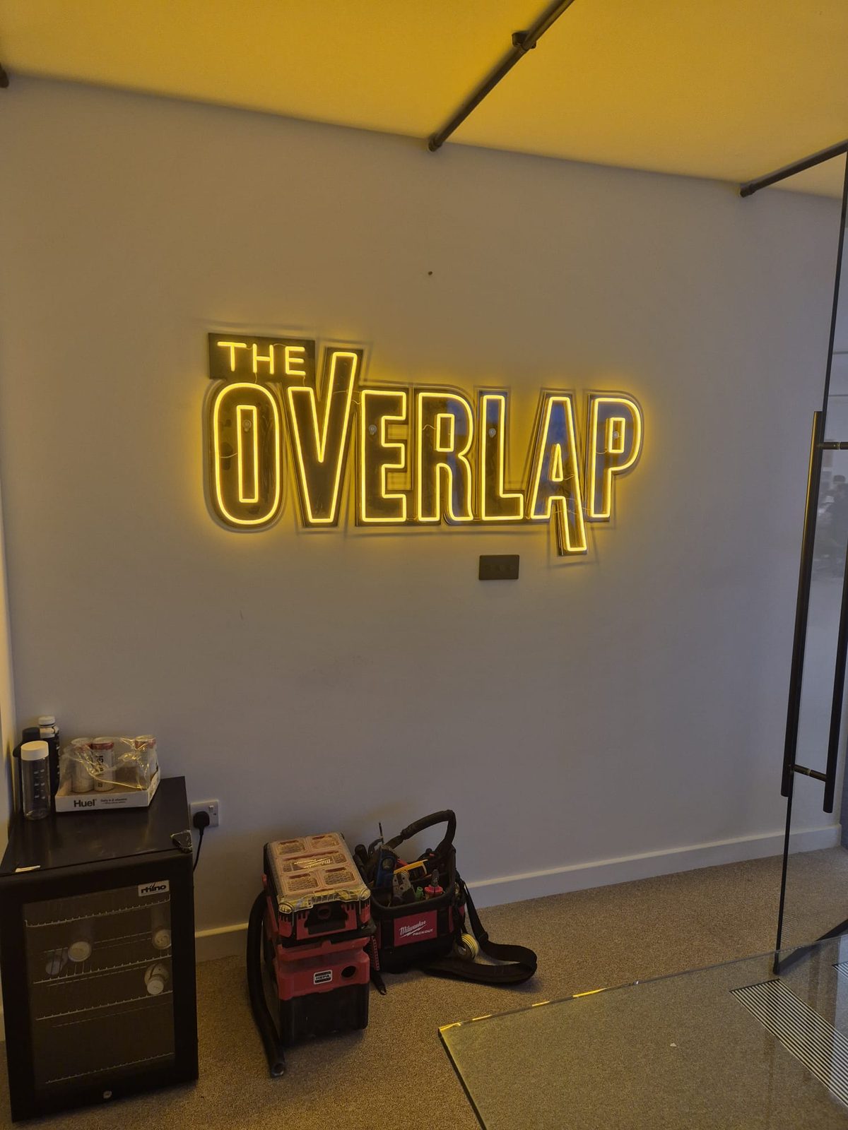 Illuminated yellow wall sign reading The Overlap above equipment