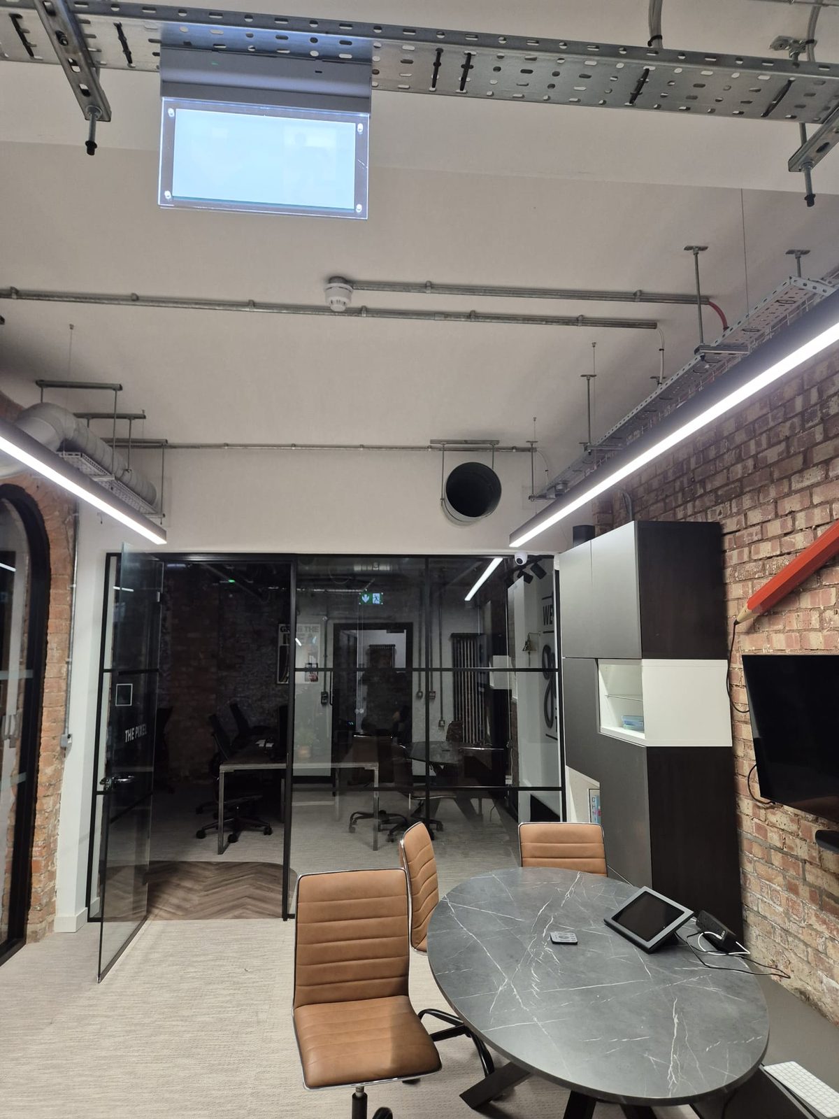 Meeting room with exposed cable tray, suspended linear lights and glass partitions