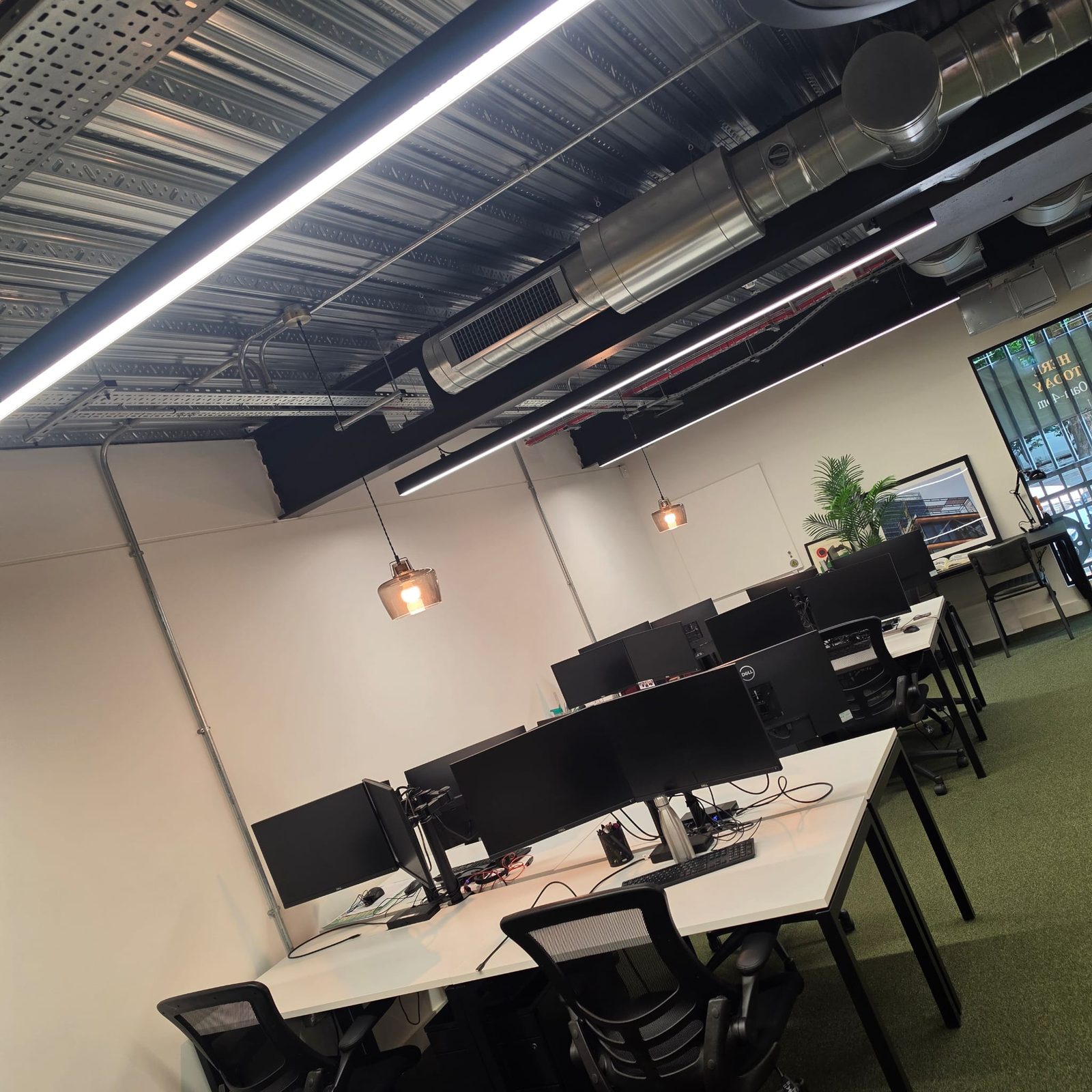 Open plan office with suspended linear lighting and exposed services above the desks