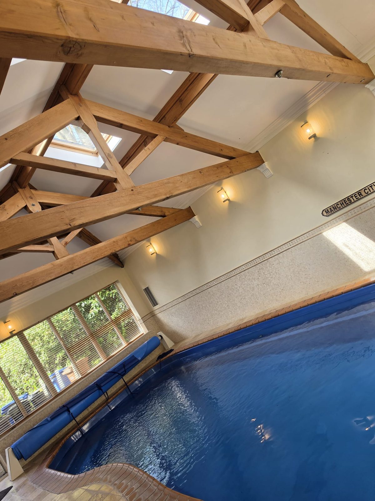 Indoor swimming pool room with timber beams, skylights and wall lighting
