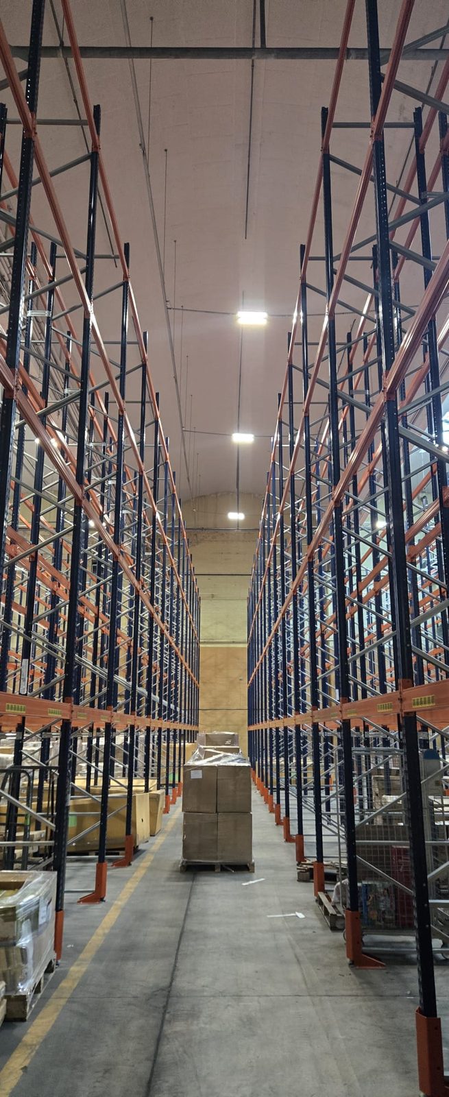 Warehouse aisle between tall racking, lit by suspended high bay fittings